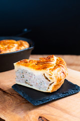 Food concept homemade pork pie or meat pie on stone plate and cast Iron Skillet on wooden background