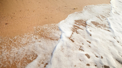 Closeup photo of sea waves rolling on beach with beautiful golden sand at sunset.