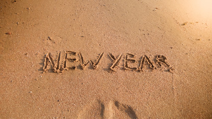 Closeup photo of words New Year written on wet sand on the sea beach. Concept of winter holidays, Christmas and tourism