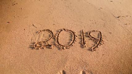 Photo of numbers 2019 written on wet sand on the sea beach. Concept of winter holidays, New Year and tourism