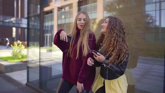two girlfriends have fun dancing on the streets of the modern city to the music from a mobile phone