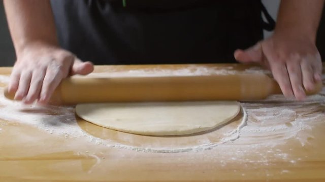 Mid-section shot of hands of unrecognizable male cook rolling and stretching pizza dough