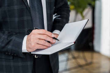 close-up partial view of businessman in formal wear writing in notebook