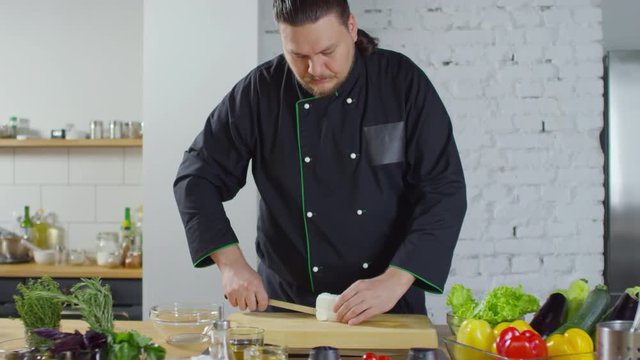 PAN shot of male restaurant chef slicing feta cheese into cubes before making salad