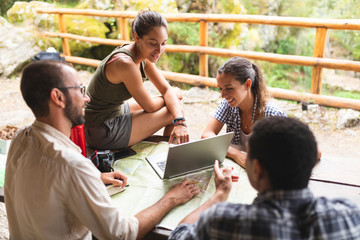 Group of hikers sitting together planning a hiking route using map and laptop