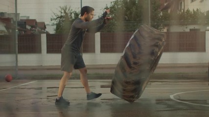 Strong Muscular Fit Young Man in Sport Outfit and Gloves is Doing Exercises in a Fenced Outdoor Basketball Court