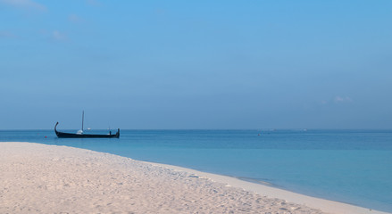 Fototapeta na wymiar white sand beach and a sail boat over turquoise lagoon in Maldives