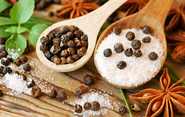 Aromatic black peppercorns in wooden spoon with pink salt and green leaves of basil are ready for cooking. Spices and herbs
