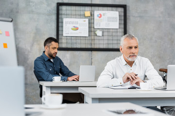 selective focus of pensive handsome businessmen sitting at table and looking away in office