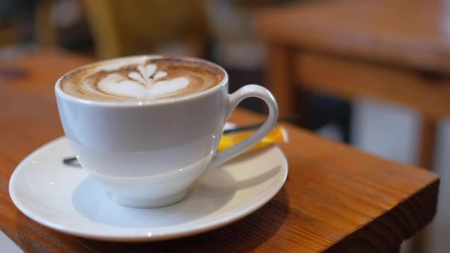 A white cup of cappuccino coffee on table with copy space for texture advertising. Royalty high-quality free stock footage of capuccino coffee with blank cup and copyspace for texture in a coffee shop