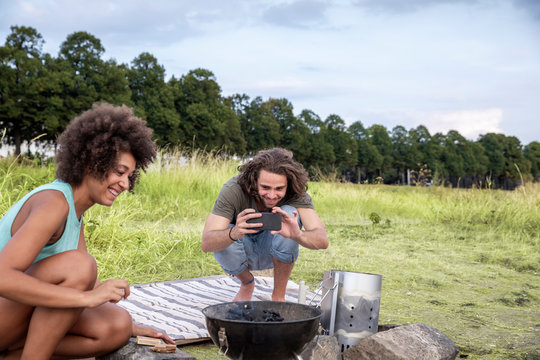 Smiling young man with girlfriend taking a picture of barbecue grill in the nature