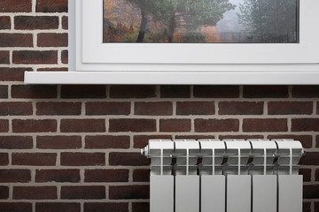 White heating radiator on the background of brown brick wall under the window