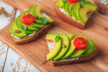 Avocado sandwich on dark rye toast bread made with fresh sliced avocado, cream cheese, seeds and cherry on white wooden background
