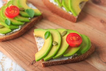 Avocado sandwich on dark rye toast bread made with fresh sliced avocado, cream cheese, seeds and cherry on white wooden background