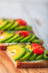 Avocado sandwich on dark rye toast bread made with fresh sliced avocado, cream cheese, seeds and cherry on white wooden background