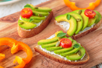 Avocado sandwich on dark rye toast bread made with fresh sliced avocado, cream cheese, seeds and cherry on white wooden background