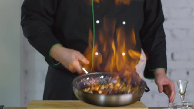 Mid section shot with tilt up of unrecognizable male restaurant chef pouring alcohol into Pan and flambeing mushrooms on high heat