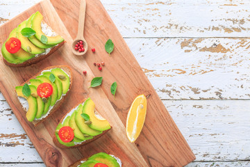 Avocado sandwich on dark rye toast bread made with fresh sliced avocado, cream cheese, seeds and cherry on white wooden background