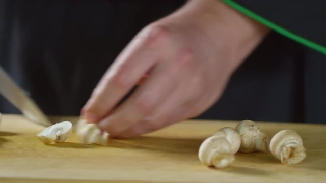 Close up tracking shot of hands of unrecognizable male cook chopping champignon mushrooms on wooden cutting board