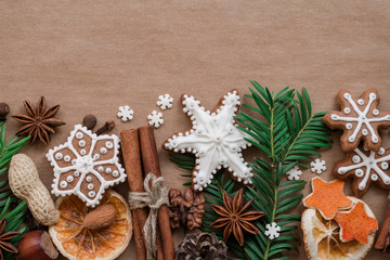 Frame with fir branches, Gingerbread cookies and Christmas decorations on dark brown paper background. Top view.