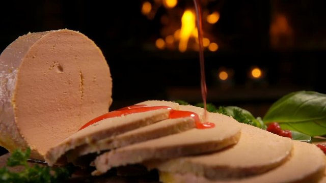 Cowberry syrup pours into pieces of foie gras pate on a plate against the background of the fireplace