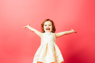 Portrait of an excited small toddler child with both arms out, isolated on pink studio background