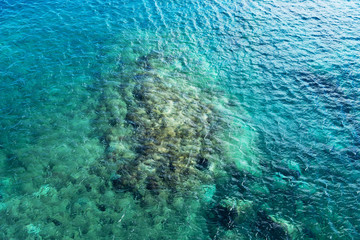 The turquoise sea background, through water the seabed stones is visible