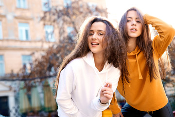 two young girls walking city having fun. joyful Women in bright colored hoodies walking, laughing...