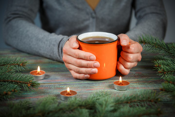 Woman holds a cup of hot tea among the fir branches and candle.