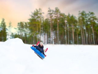 winter, leisure and entertainment concept - happy teenage girl sliding down hill on snow tube