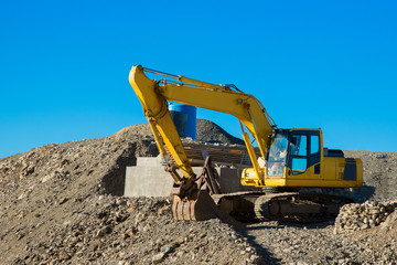 The excavator rakes in stones with his bucket. Excavator rakes rocky ground. Yellow excavator in work.