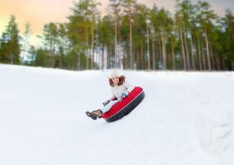 Fototapeta na wymiar winter, leisure and entertainment concept - happy teenage girl sliding down hill on snow tube