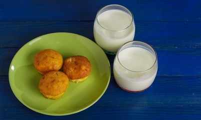 Cottage cheese cakes on a plate and two glasses of milk on the table.