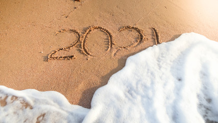 Closeup image of 2021 numbers being washed from wet sand on beach by the sea wave. Concept of New Year, Christmas and travel on winter holidays.