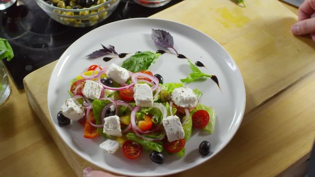 Handheld high angle shot of hands of unrecognizable restaurant chef plating Greek salad and decorating it with basil leaves