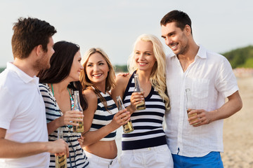 friendship, summer holidays and people concept - group of happy friends in striped clothes drinking non alcoholic beer on beach