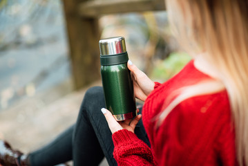 beautiful happy girl in a red sweater with a thermos outdoors, a woman is resting in nature