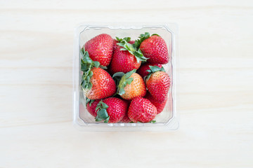 Fresh red strawberries in plastic container with wooden background : Top view