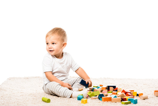 cute toddler boy smiling and playing with wooden blocks on carpet isolated on white