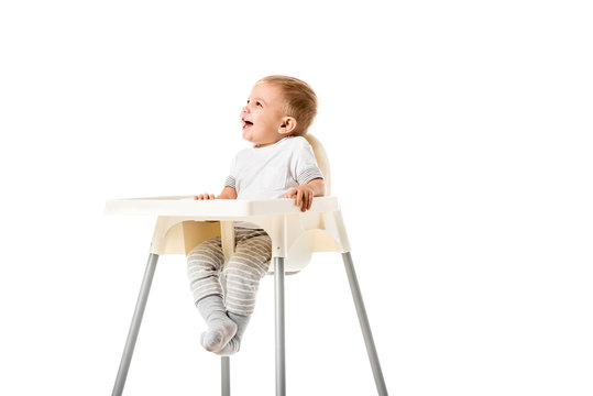 happy toddler boy smiling and sitting in highchair isolated on white