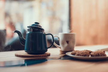 Laconic image of the ceramic cup standing near the teapot with steam over the table