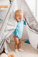 cute toddler boy in blue bodysuit standing in grey baby wigwam on carpet © LIGHTFIELD STUDIOS