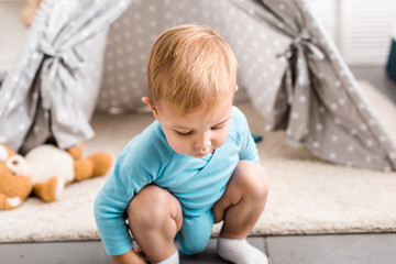 cute toddler boy in blue bodysuit sitting on hunkers near grey wigwam © LIGHTFIELD STUDIOS