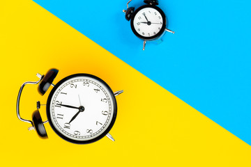 Black alarm clock on color block yellow and blue background