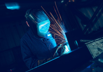  A vibrant action shot of a skilled working metal welder in action, welding metal. Photographed with a slow shutter speed and spark trails. Orange and teal. - obrazy, fototapety, plakaty