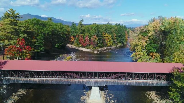 Sunny rising shot of covered bridge in the fall with people to reveal mountains