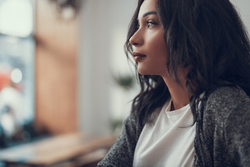 Peaceful young dark haired woman sitting alone and thoughtfully looking into the distance
