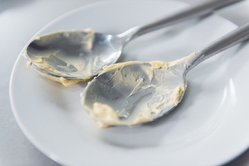 empty sticky spoons full of cake dough and butter, resting on an empty white plate.. Beautiful depth of field and creamy soft environment.