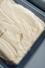 A close up of An industrial kitchen food mixing machine whipping and mixing sweet creamy fluffy light cake mixture, in a silver metal bowl.