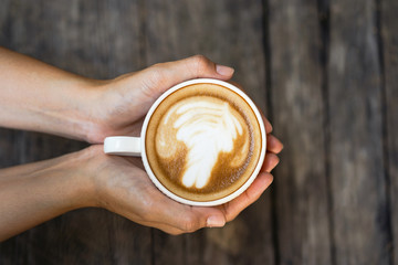 Female hands holding cup of coffee on wooden table background